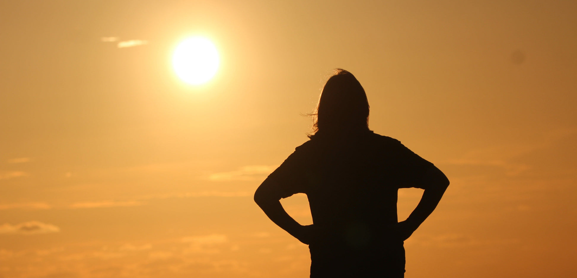 Person standing with hands on hips against a sunset sky